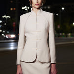 A professional woman wearing a sophisticated beige modern Qipao-inspired skirt suit, featuring a tailored blazer with traditional Chinese frog buttons and a stand collar for an elegant executive office look.