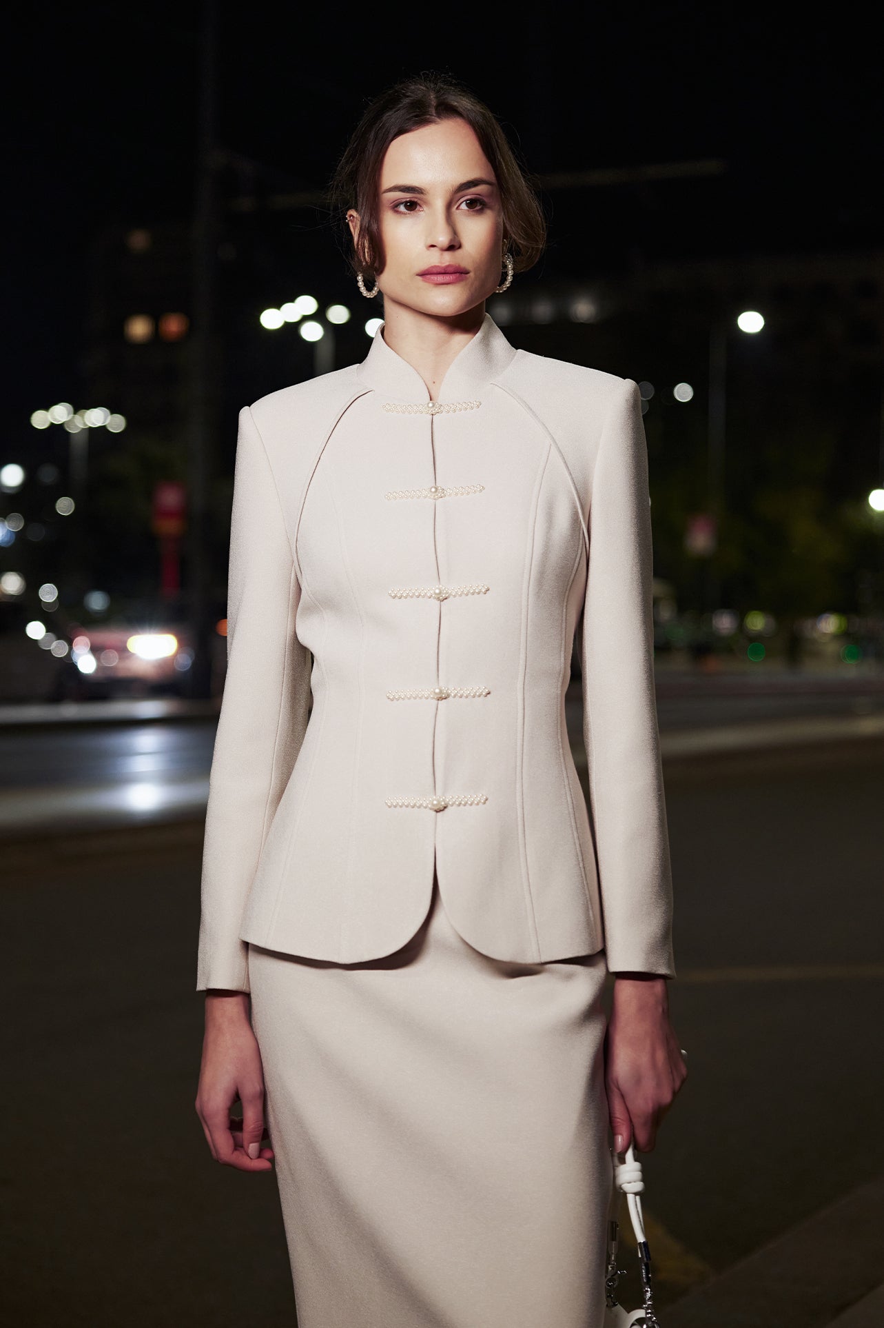 A professional woman wearing a sophisticated beige modern Qipao-inspired skirt suit, featuring a tailored blazer with traditional Chinese frog buttons and a stand collar for an elegant executive office look.