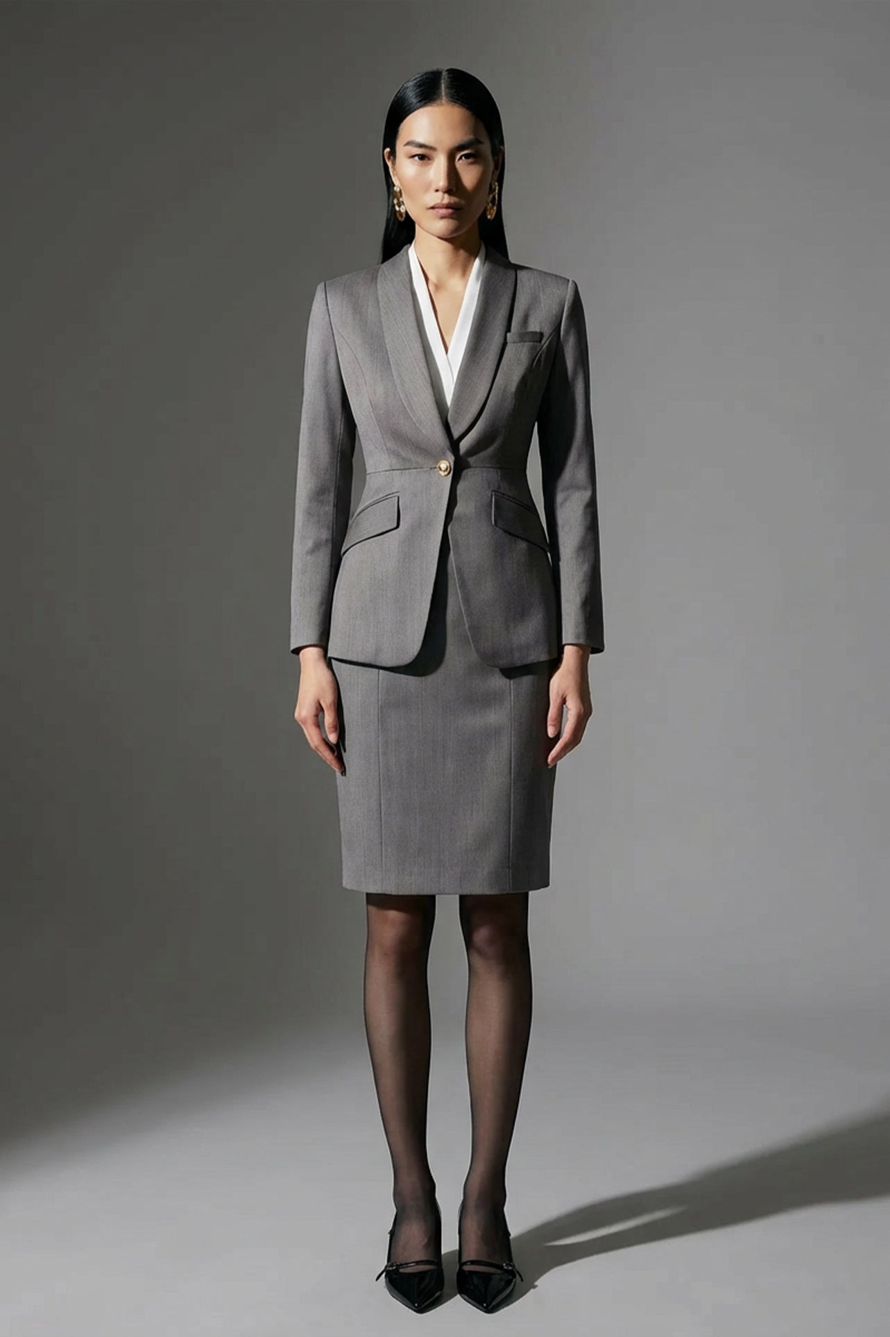 A professional woman wearing a sophisticated grey slim-fit blazer with a single gold button, featuring a tailored waist and notched lapels for an elegant executive office look.