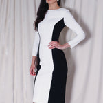 A professional woman wearing a sophisticated black and white color-block midi dress, featuring slimming side panels, long sleeves, and an elegant black belt with a gold buckle for a modern executive office look.