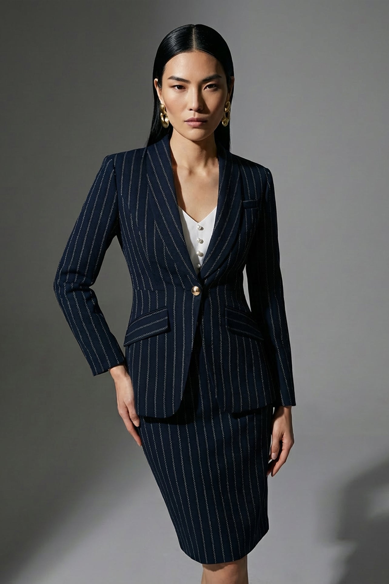 A professional woman wearing a sophisticated navy blue pinstripe suit, featuring a tailored single-button blazer and a matching midi pencil skirt with a front slit for an elegant executive office look.
