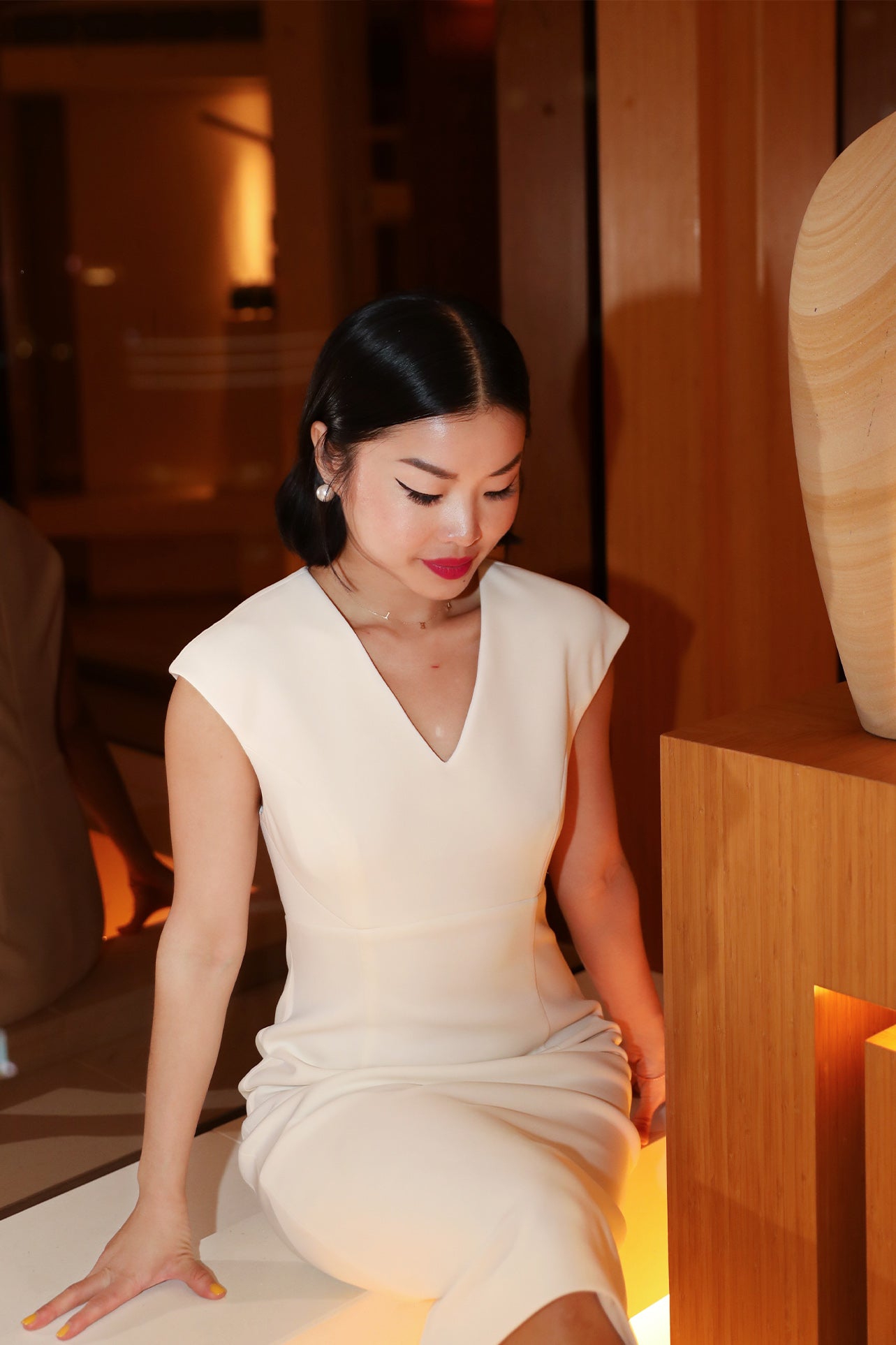 A professional woman wearing a sophisticated solid white sleeveless sheath dress, featuring a flattering V-neckline and an elegant thin black belt with a gold buckle for a polished executive office look.