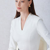 A professional woman wearing a sophisticated solid white long-sleeve sheath dress, featuring an elegant V-neckline and a slim black belt with a gold buckle for a polished executive office look.