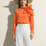 A style collection of three models presenting elegant dopamine office wear; the left in a white bow-tie blouse with a mustard yellow front-slit midi skirt, the center wearing a blue striped pussy-bow shirt with a straw hat and white wide-leg trousers, and the right in a vibrant orange satin blouse with a royal blue pencil skirt.