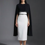 Two professional women wearing sophisticated cape-style dresses: one in a classic black and white monochrome with a thin belt, and the other in a vibrant magenta pink, perfect for a powerful and elegant evening look.