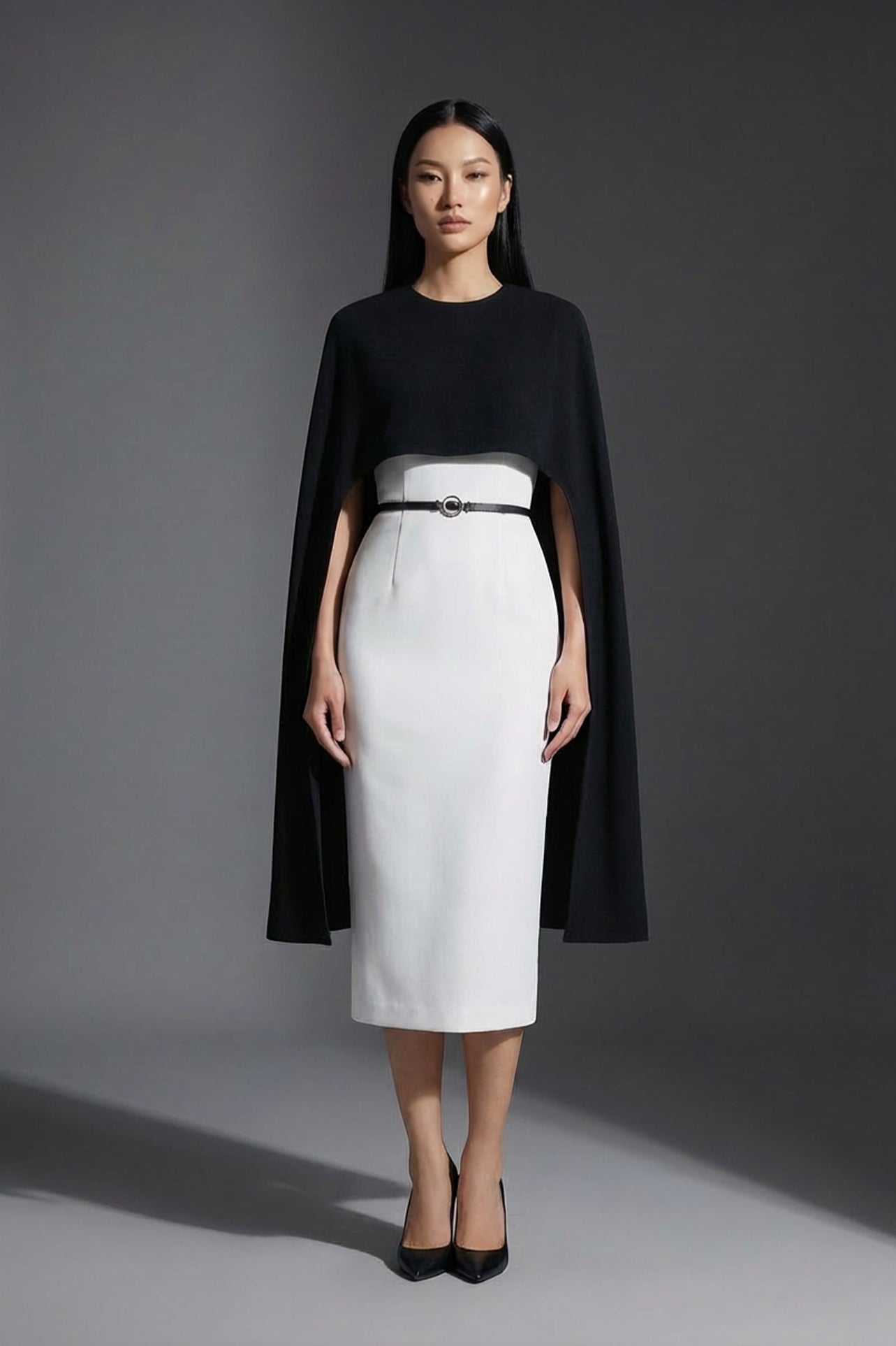 Two professional women wearing sophisticated cape-style dresses: one in a classic black and white monochrome with a thin belt, and the other in a vibrant magenta pink, perfect for a powerful and elegant evening look.