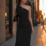 A style comparison of two elegant one-shoulder midi dresses; the left showcasing a sophisticated beige tailored sheath dress with a large tie-bow shoulder strap, and the right featuring the same design in timeless minimalist black.