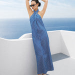 A model showcasing an elegant blue and white vertical striped maxi dress, featuring a sophisticated criss-cross halter neckline, a structured wide banded waist for a slimming silhouette, and a long flowing skirt, paired with white strap high heels.