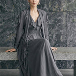 A style comparison of two elegant long-sleeve chiffon maxi dresses; the left showcasing a vibrant purple dress with a deep V-neckline and tiered ruffles along the sleeves, and the right featuring a sophisticated grey version styled with a matching neck scarf and smocked waistband.