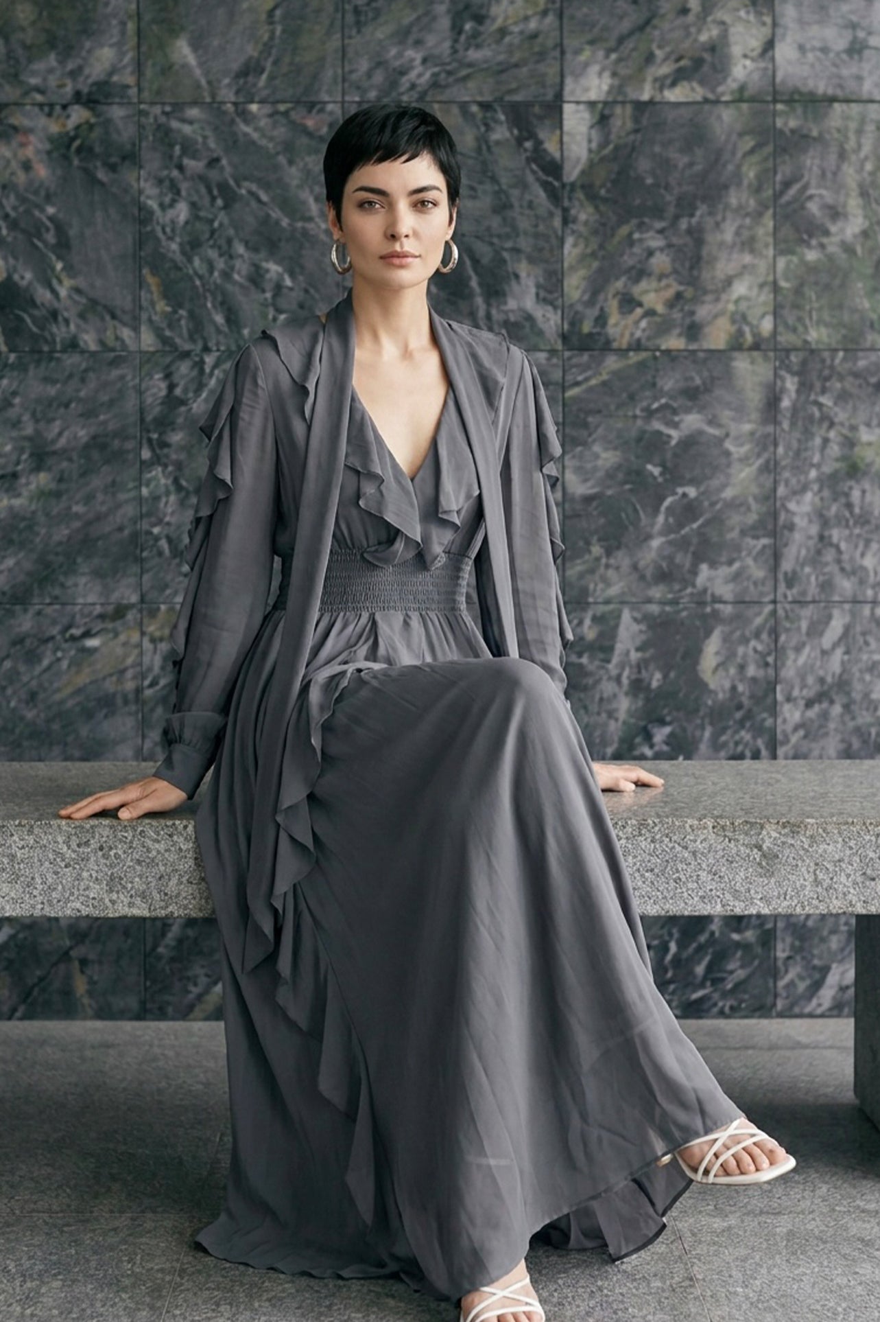 A style comparison of two elegant long-sleeve chiffon maxi dresses; the left showcasing a vibrant purple dress with a deep V-neckline and tiered ruffles along the sleeves, and the right featuring a sophisticated grey version styled with a matching neck scarf and smocked waistband.