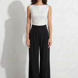 A professional woman modeling an elegant color-block lace sheath dress, featuring a sleeveless white lace bodice with a 3D flower applique on a bateau neckline and a tailored navy blue lace pencil skirt.