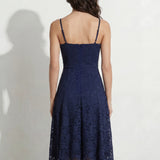 A professional woman modeling an elegant navy blue lace midi dress, featuring delicate V-neck spaghetti straps, a tailored fit-and-flare silhouette, and a beautiful flowing asymmetric handkerchief lace trim hem.