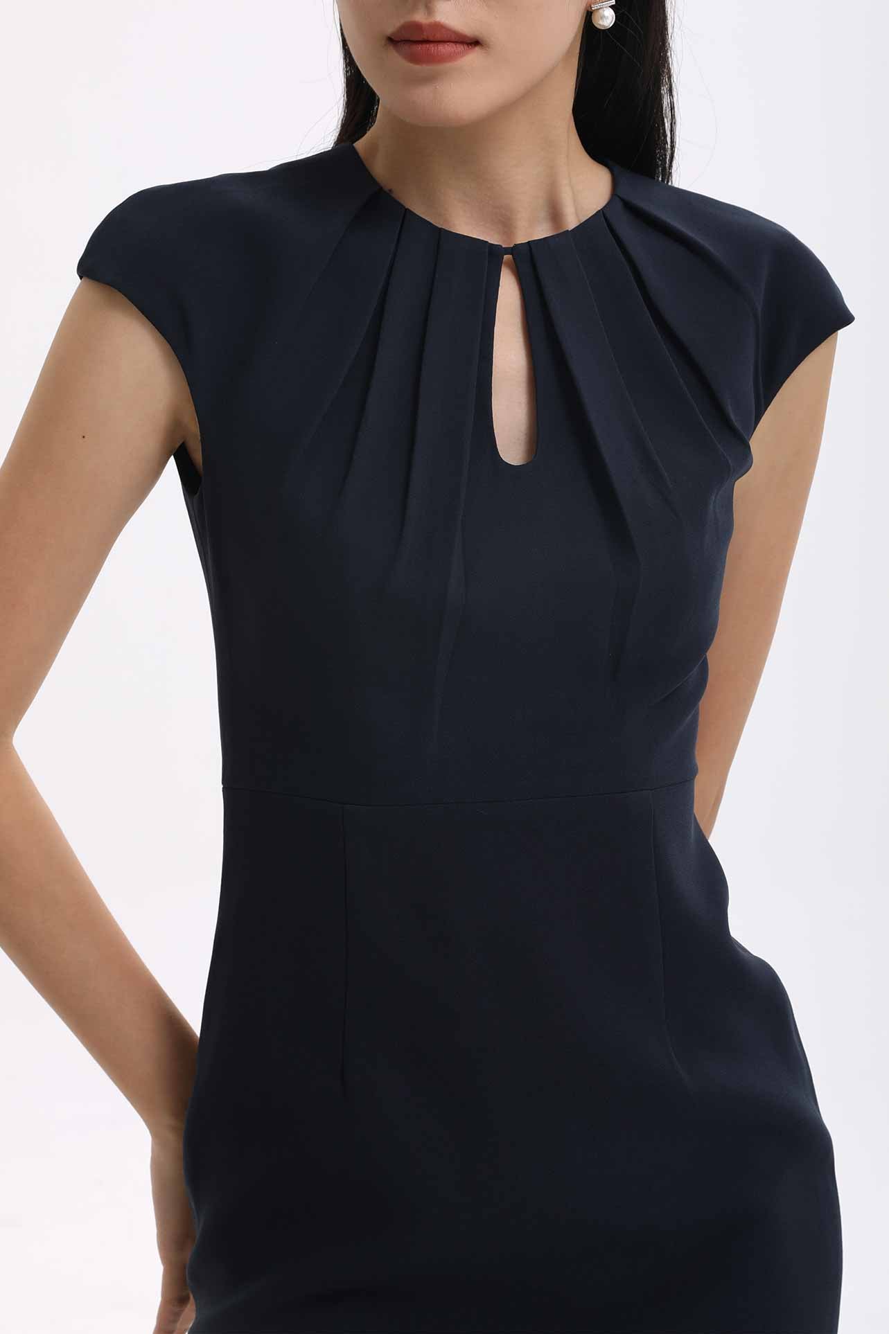 A professional woman wearing a sophisticated navy blue midi dress, featuring an elegant pleated neckline with a subtle keyhole detail and a tailored slim-fit pencil silhouette for a polished executive look.