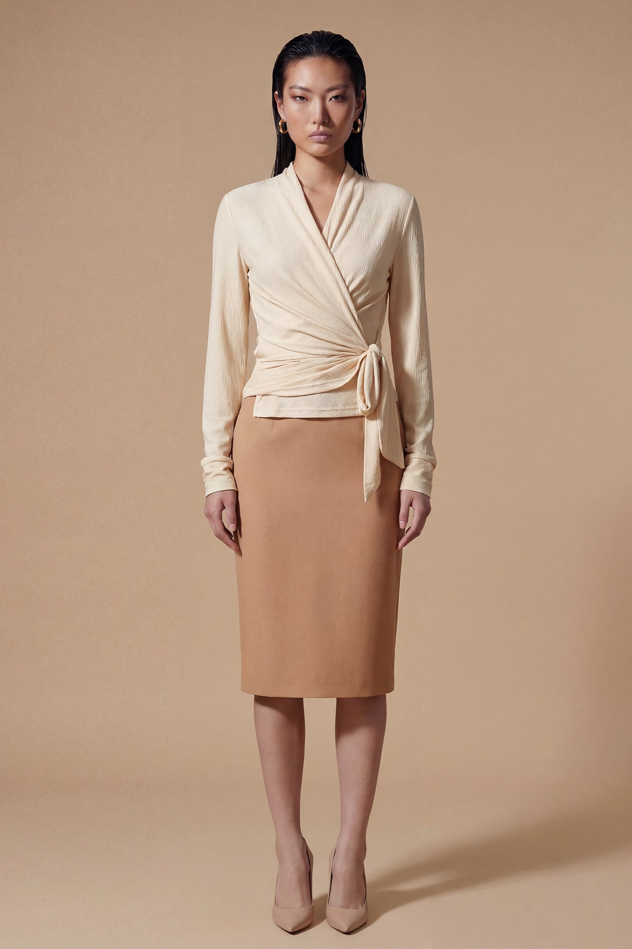 Two models presenting versatile textured wrap tops in cream and dark chocolate, featuring a slimming V-neck and elegant side-tie waist, styled with a tan pencil skirt and white high-waisted trousers.
