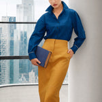A style comparison of two elegant long-sleeve button-down work shirts with refined cuff stitching; the left in vibrant mustard yellow tucked into a grey pinstripe pencil skirt, and the right in royal blue paired with flowing white wide-leg trousers.