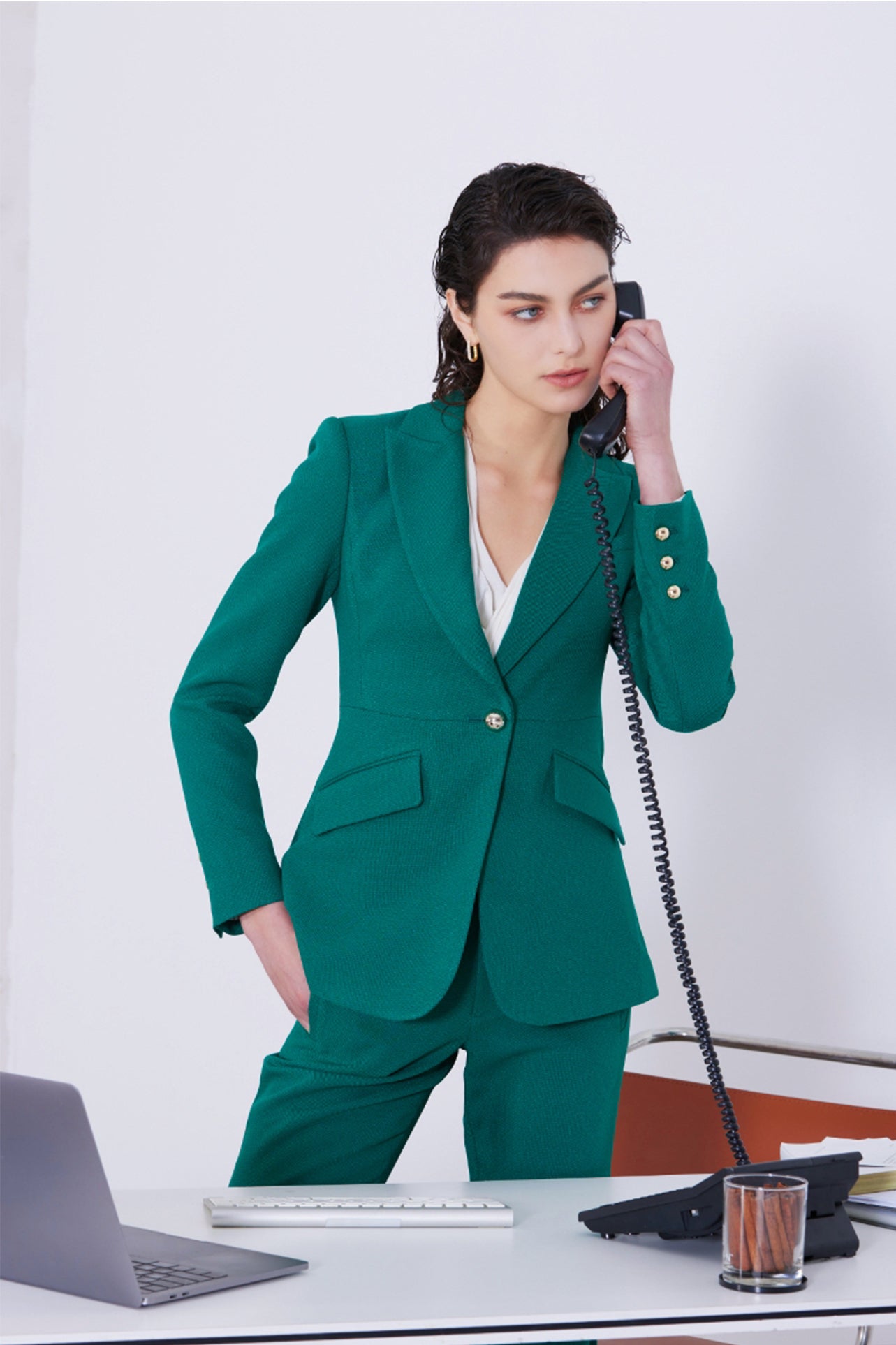 A professional woman wearing a sophisticated emerald green tailored blazer, featuring a slim-fit silhouette, notched lapels, and flap pockets, styled elegantly with a patterned silk scarf for a corporate office look.