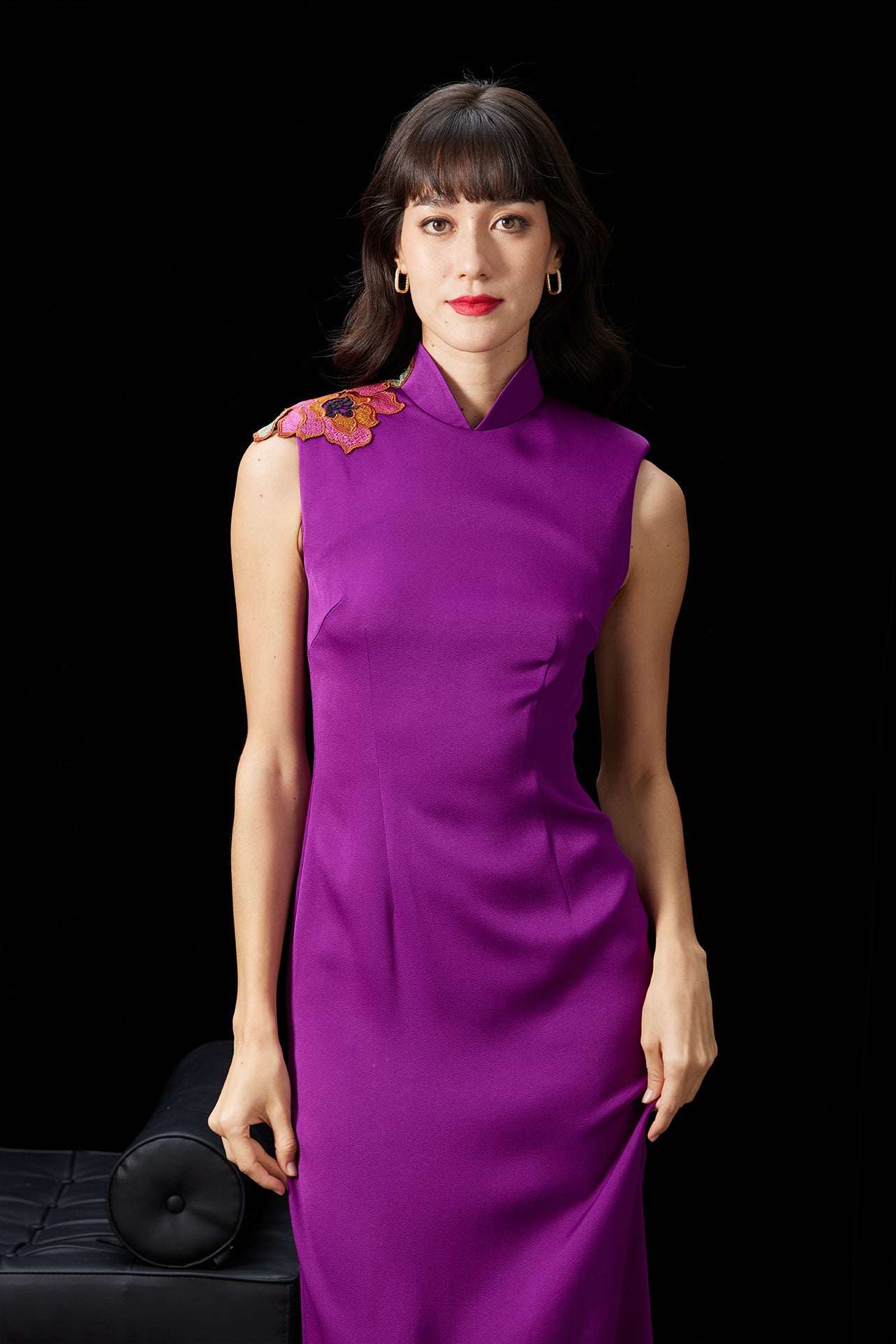 A professional woman wearing a stunning purple satin sleeveless dress, featuring a traditional mandarin collar and delicate floral embroidery on the shoulder for a modern oriental-inspired formal look.