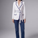 An elegant professional woman wearing a tailored white blazer with navy blue contrast piping, featuring a self-tie belt to define the waist for a smart-casual office look