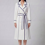 An elegant professional woman wearing a sophisticated white double-breasted coat dress featuring sharp navy blue contrast piping and a matching waist belt for a tailored executive look