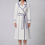 An elegant professional woman wearing a sophisticated white double-breasted coat dress featuring sharp navy blue contrast piping and a matching waist belt for a tailored executive look