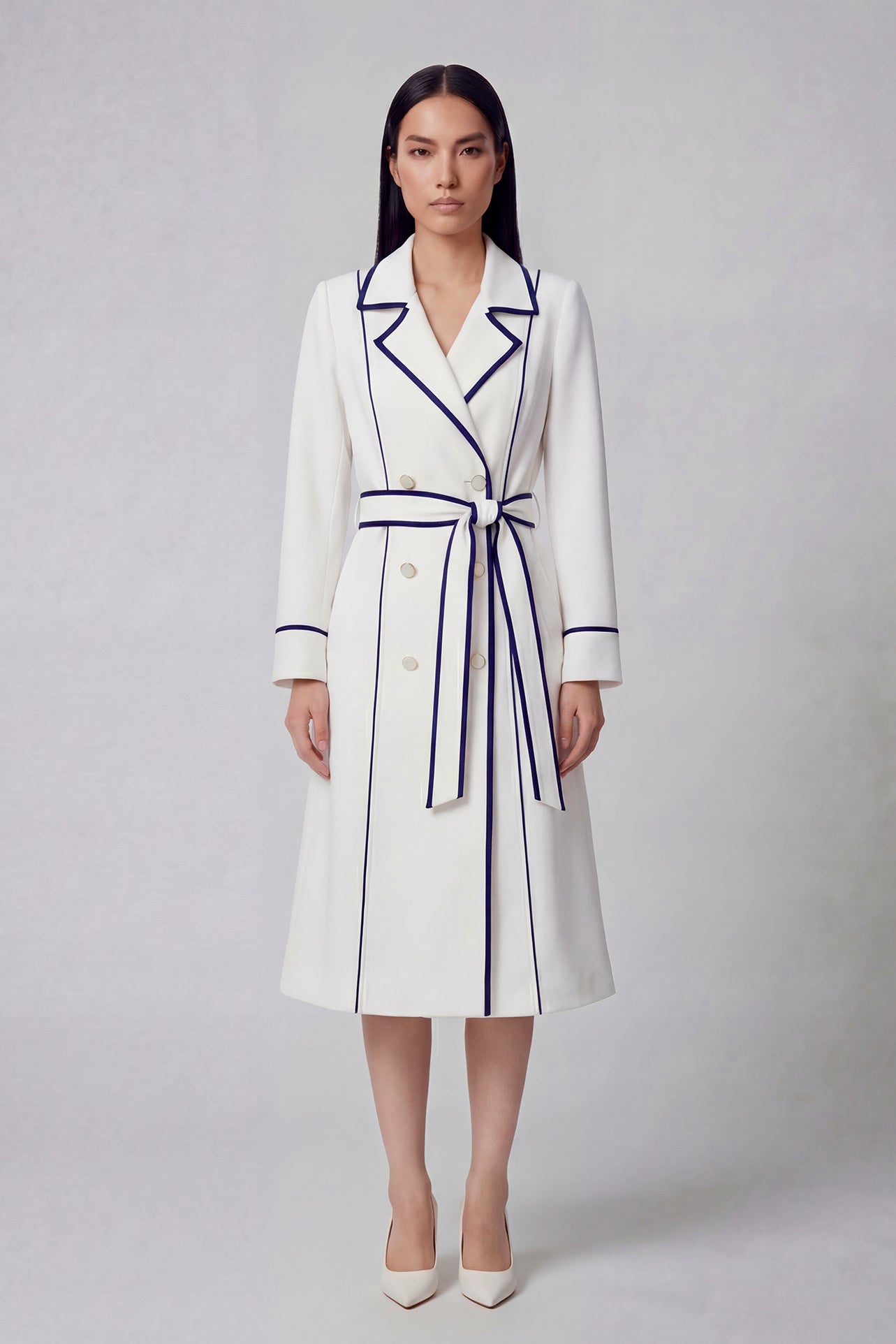 An elegant professional woman wearing a sophisticated white double-breasted coat dress featuring sharp navy blue contrast piping and a matching waist belt for a tailored executive look