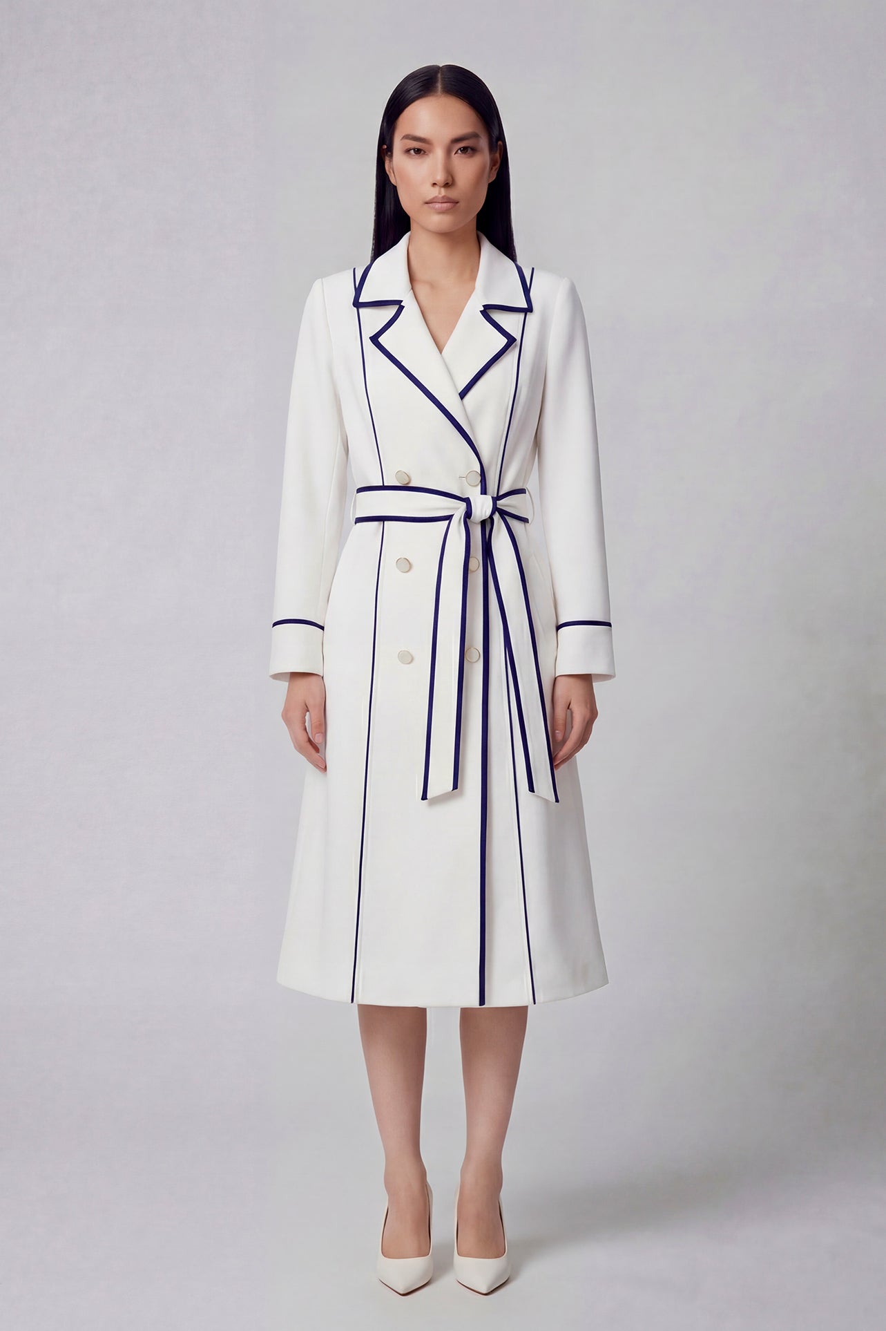 An elegant professional woman wearing a sophisticated white double-breasted coat dress featuring sharp navy blue contrast piping and a matching waist belt for a tailored executive look