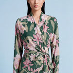 A professional woman wearing a sophisticated dark green wrap dress with a vibrant pink floral print, featuring long sleeves and a slimming waist-tie for an elegant spring look.