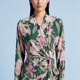 A professional woman wearing a sophisticated dark green wrap dress with a vibrant pink floral print, featuring long sleeves and a slimming waist-tie for an elegant spring look.